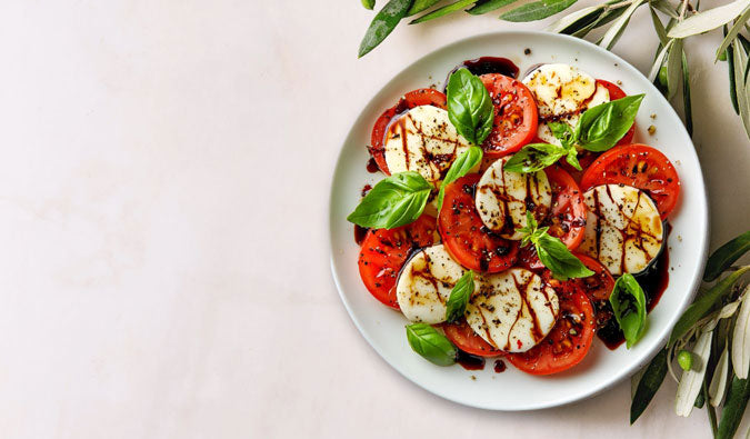 Caprese salad with tomatoes, mozzarella, and basil on a white plate with olive branches.