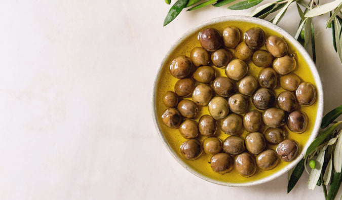 White bowl filled with fresh olives marinating in fresh extra virgin olive oil on a light background