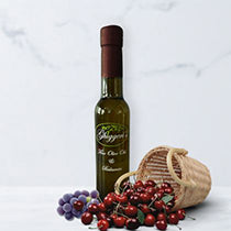 Bottle of dark balsamic vinegar with a small basket of fresh cherries and green grapes on a light gray background