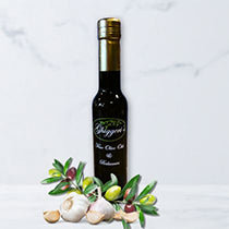 Bottle of olive oil with fresh garlic cloves and olive branches on a light background