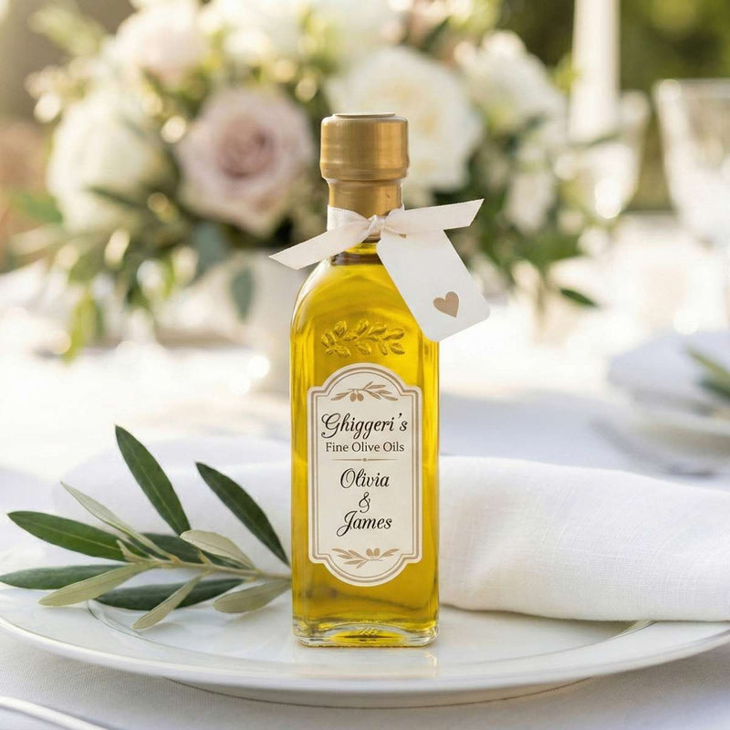 Single Ghiggeris custom label olive oil wedding favor bottle with a white ribbon, displayed on a dinner plate with a fresh olive branch