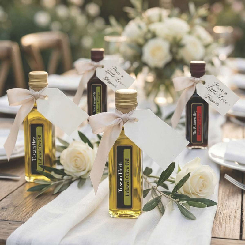 Wedding reception table setting featuring assorted Ghiggeris mini olive oil and balsamic vinegar bottles as guest favors, decorated with white bows and greenery