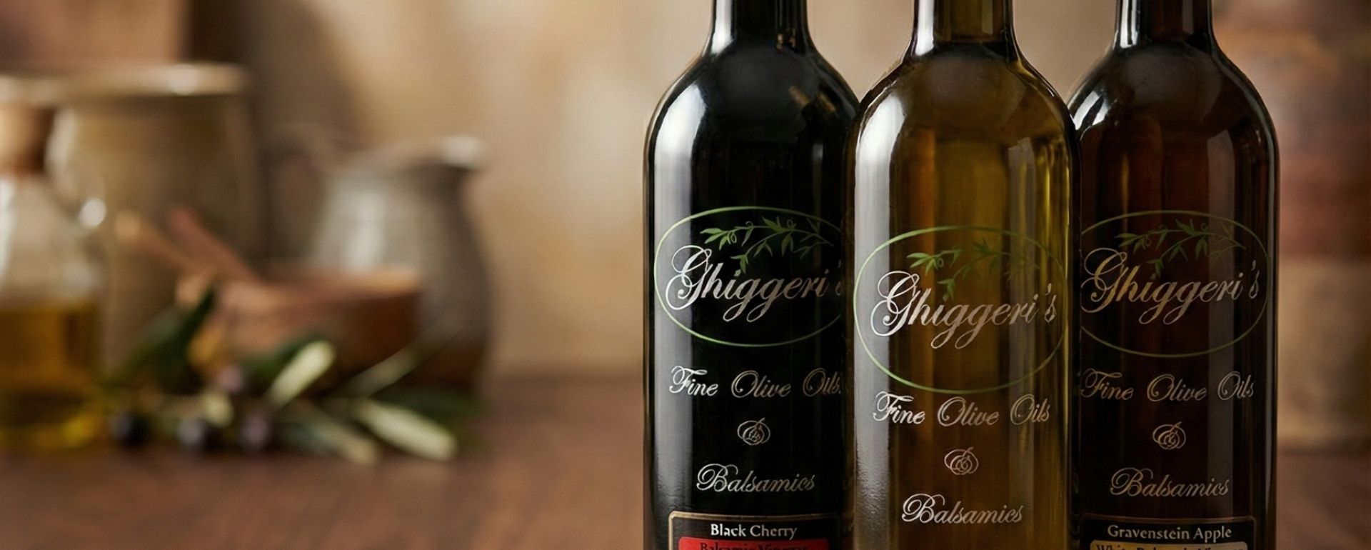 Close-up of premium Ghiggeri's Black Cherry and Gravenstein Apple balsamic vinegar bottles, showcasing elegant labeling and dark glass packaging for a luxury corporate gifting header