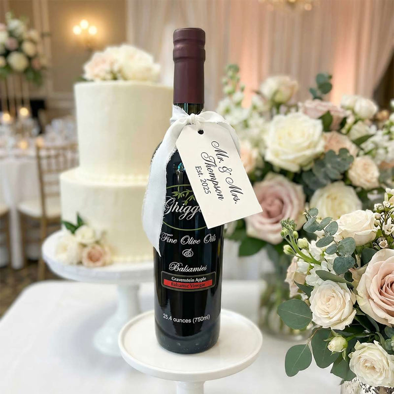 Premium Ghiggeris balsamic vinegar bottle with a custom 'Mr. & Mrs.' tag, displayed on a pedestal next to a tiered wedding cake.