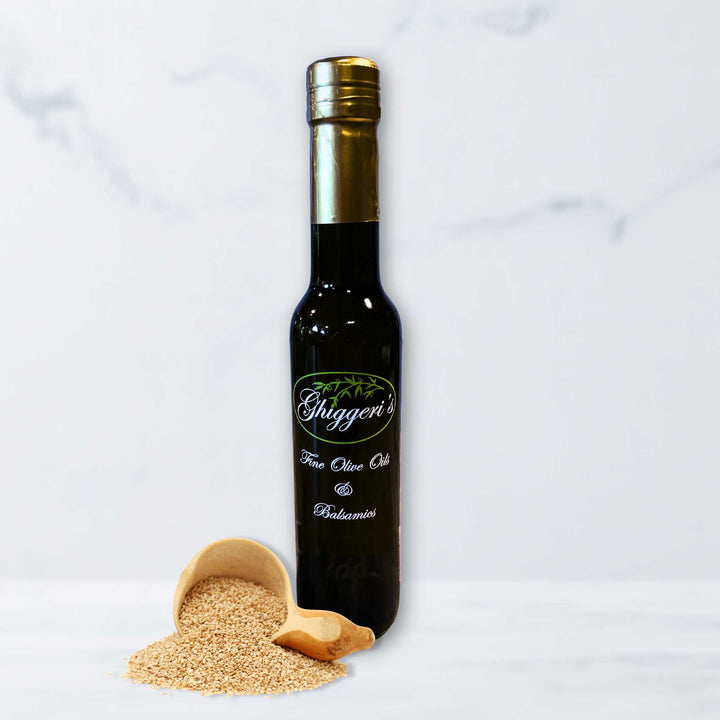 A bottle of Ghiggeri's toasted sesame seed oil with scattered sesame seeds on a natural stone surface.