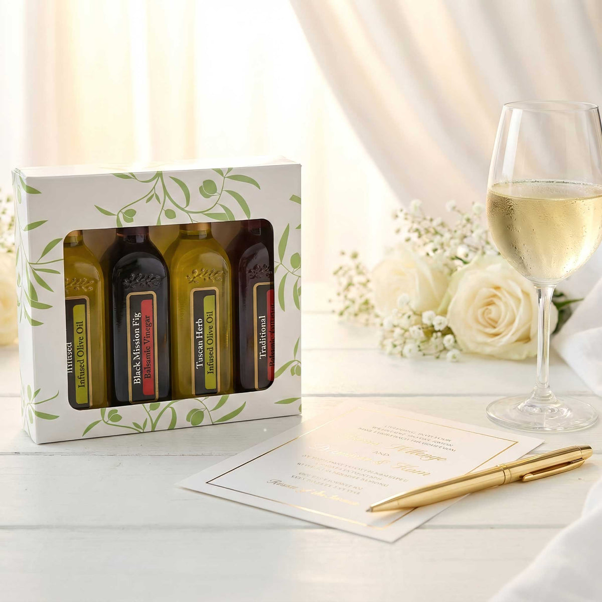 Ghiggeris wedding favor sampler pack containing four mini olive oil and balsamic bottles, displayed in a rustic box next to a glass of white wine and wedding invitation