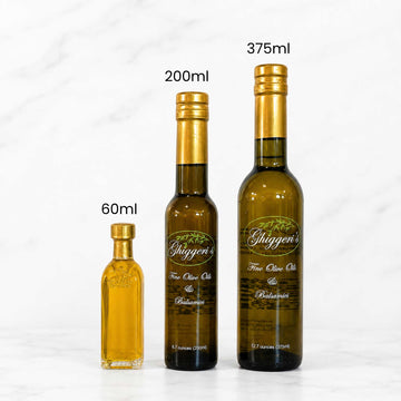 Three bottles of Shiggen's Extra Virgin Olive Oil in different sizes (60ml, 200ml, and 375ml) arranged on a white marble surface with text labels indicating their capacities.