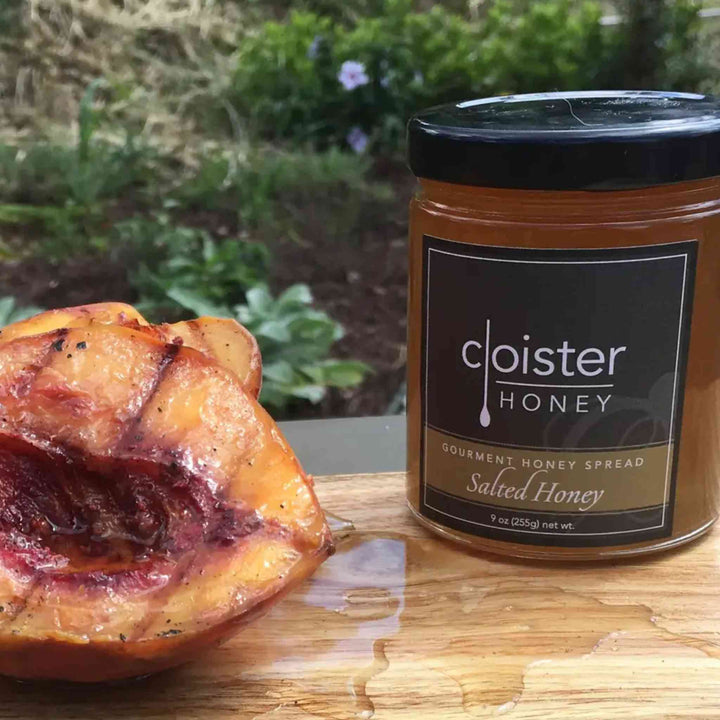 Jar of cloister honey with a honey-covered peach on a wooden surface outdoors.